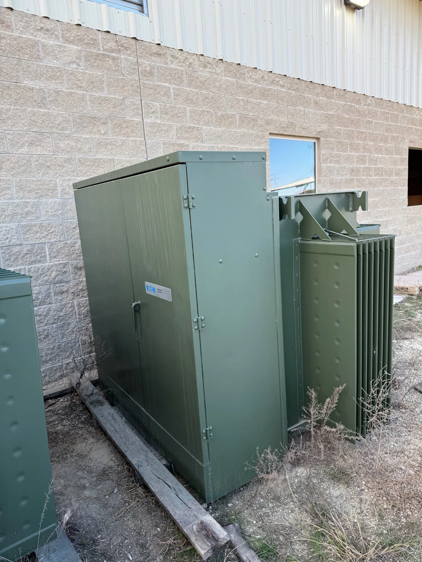 Green pad-mounted transformer beside an industrial building